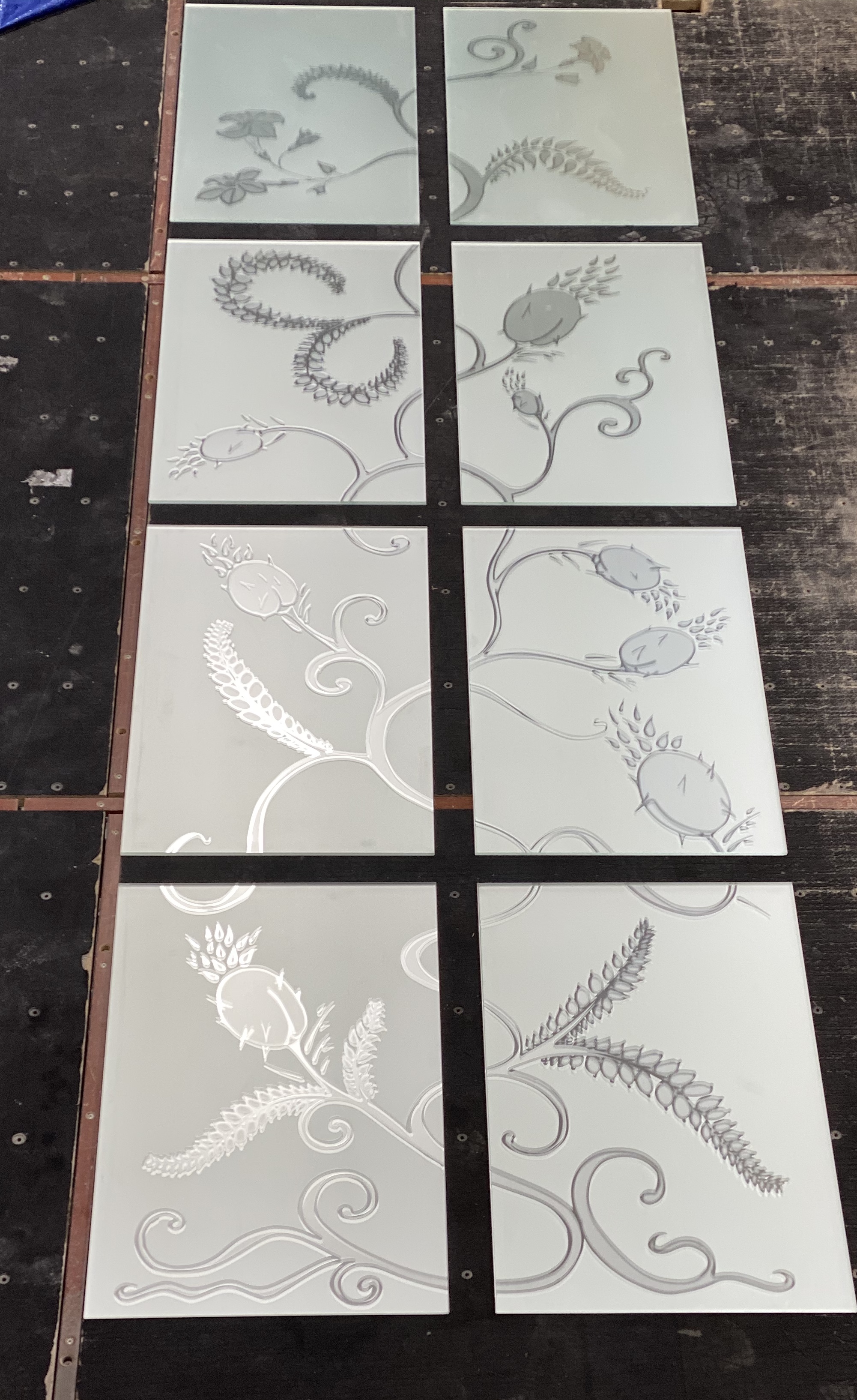 Eight sandblasted floral glass panels laid out on the workshop floor