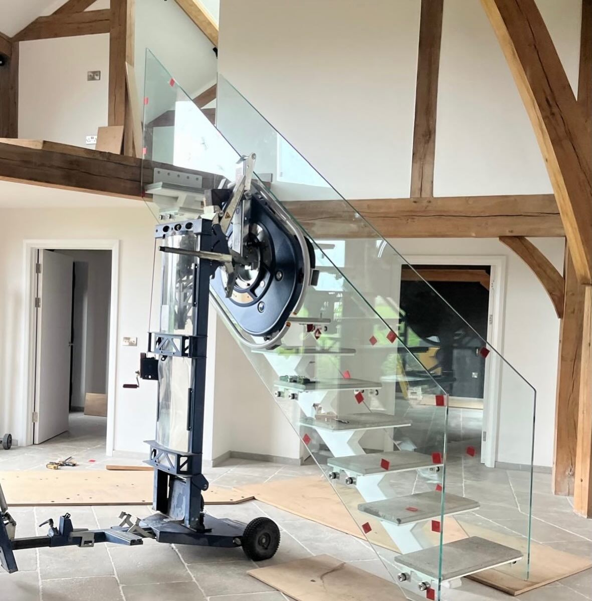 Frameless glass staircase balustrade being fitted with a glass lifting robot in an oak beamed barn